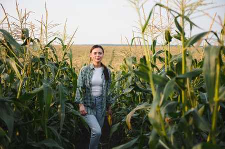 Pretty young farmer woman in corn field in early summer and checking the quality of leaves.