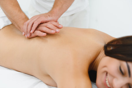 Osteopath massaging back of woman lying on front in health spa.の写真素材