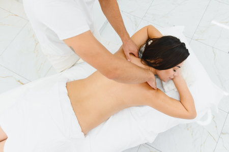 Woman enjoying professional body massage at a modern spa salon. Relaxed young lady lying on a massage table while a skilled masseur is gently massaging her back. Beauty, health, pleasure, concept.の写真素材