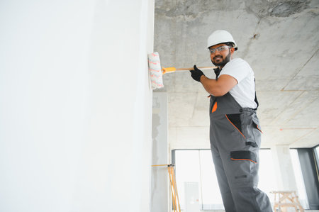 An Indian apartment repair worker paints a white wall with a roller.の写真素材