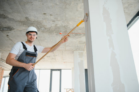 Side view of painter man painting the wall, with paint roller on big empty space. Copy space. Bannerの写真素材