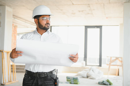 Portrait of young handsome Indian male civil engineer or architect wearing helmet at construction...