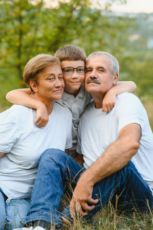 Grandparents with their grandson. They playing on meadow and joying in sunset.の写真素材