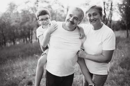 Grandson, grandfather and grandmother sitting on grass having fun outdoors in park at sunset.の写真素材