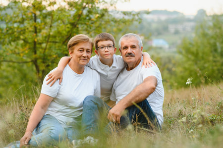 Grandparents with their grandson. They playing on meadow and joying in sunset.