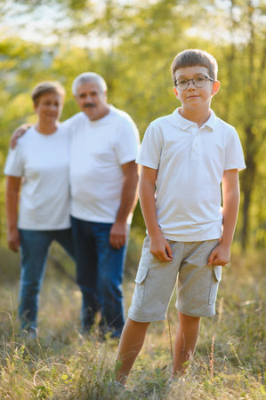 Grandson, grandfather and grandmother are standing on grass in a park at sunset.の写真素材