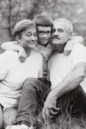 Grandson, grandfather and grandmother sitting on grass having fun outdoors in park at sunset.の写真素材
