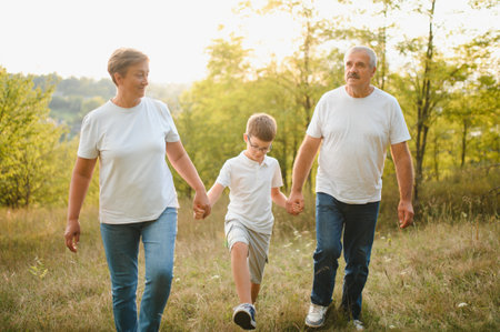 Grandson, grandfather and grandmother sitting on grass having fun outdoors in park at sunset.