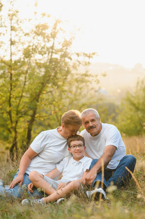 Grandparents with their grandson. They playing on meadow and joying in sunset.の写真素材
