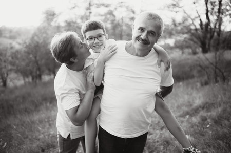 Grandson, grandfather and grandmother sitting on grass having fun outdoors in park at sunset.の写真素材