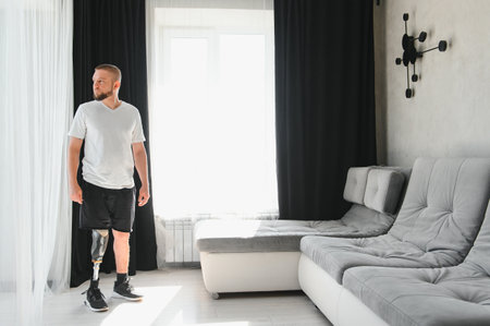 Man amputee with prosthetic leg disability on above knee transfemoral leg prosthesis artificial device at home. People with amputation disabilities everyday life.の写真素材
