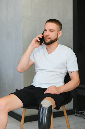 A young man with a prosthetic leg is sitting at home and talking on the phone.の写真素材