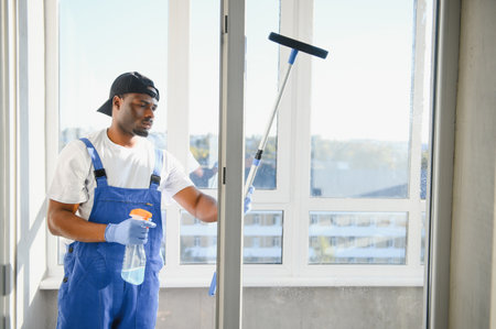 African Male professional cleaning service worker in overalls cleans the windows and shop windows of a store with special equipment.の写真素材