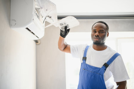 African American electrician repairing air conditioner indoors.の写真素材