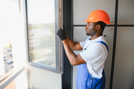 Young African Repairman In Overalls Installing Window.の写真素材