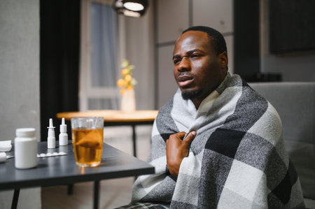 rhinitis, medicine and healthcare concept sick african american man in blanket using nasal spray at home.の写真素材
