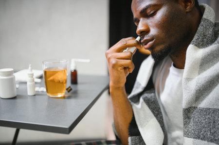 Man using nasal spray for relief from allergies or cold, sitting in a cozy home setting.の写真素材