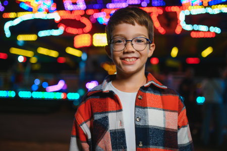 A child enjoying an evening at an amusement park, wearing a plaid shirt and glasses, with colorful lights in the backgroundの写真素材