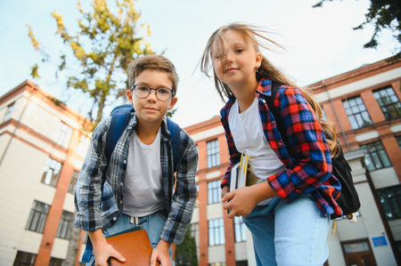 Happy school kids friends boy and girl with backpacks walking and laughing having fun together near school building outside outdoor after lessons.の写真素材