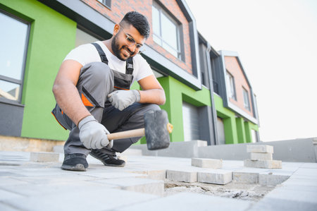 Indian Worker skillfully laying paving stones using a hammer and wearing gloves, showing precision.の写真素材