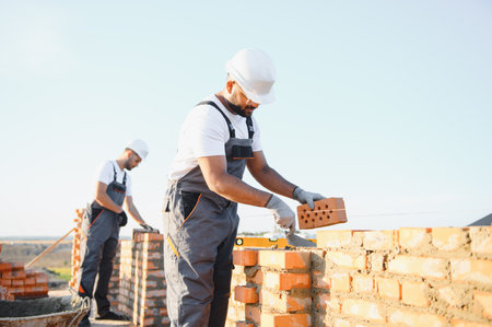 A team of construction workers in overalls and hard hats are building a brick wall.