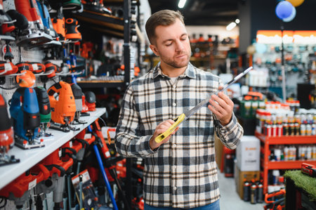 Portrait of young bearded man choosing saw on tree in hardware store.の写真素材