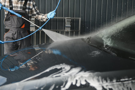 Man worker washing car service. Car wash station high pressure water. Employees clean a vehicle professionally.の写真素材
