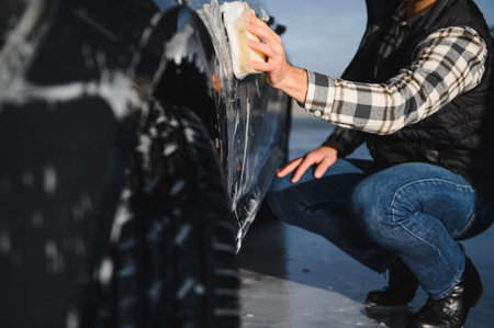 Man washing car service with foam and sponge. Car wash cleaning wipe station. Employees clean a vehicle professionally.の写真素材