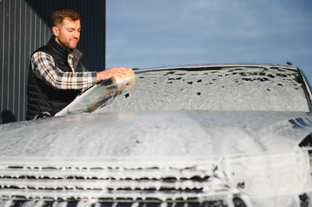 Man washing car service with foam and sponge. Car wash cleaning wipe station. Employees clean a vehicle professionally.の写真素材