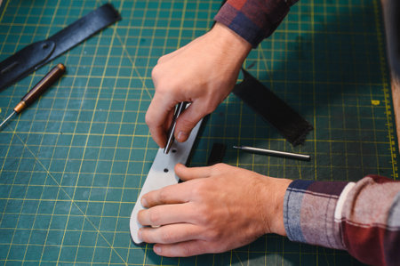 male artisan carefully punching piece of leather at professional leather workshop.の写真素材