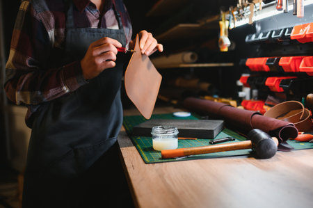 male artisan carefully punching piece of leather at professional leather workshop.の写真素材