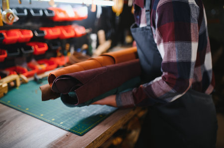 Tailor cobbler hold different rolls natural brown leather, working in workshop. Concept banner...