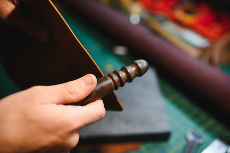 Production process. Young focused experienced master craftsman makes leather goods at his workplace.
