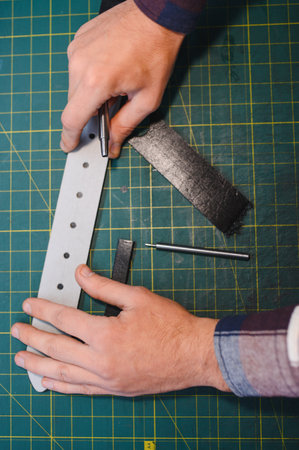 Working process of the leather belt in the leather workshop. Man holding crafting tool and working.