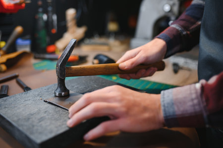 Production process. Young focused experienced master craftsman makes leather goods at his workplace.の写真素材