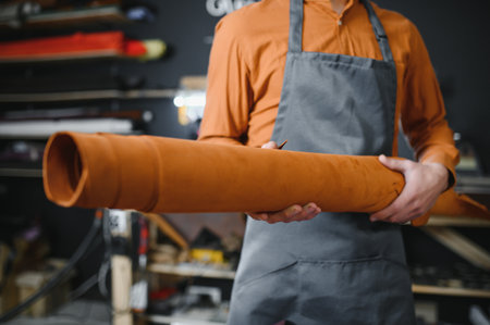 professional crafter checking the material at workplace,artisan checks the quality of a roll of genuine leather for sewing clothes, shoes and accessories made of leather.の写真素材