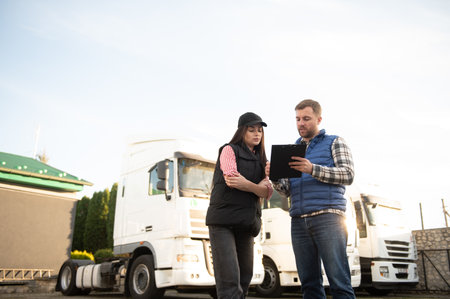 Logistics - proud driver or forwarder and female coworker, in front of trucks and trailers, on a...