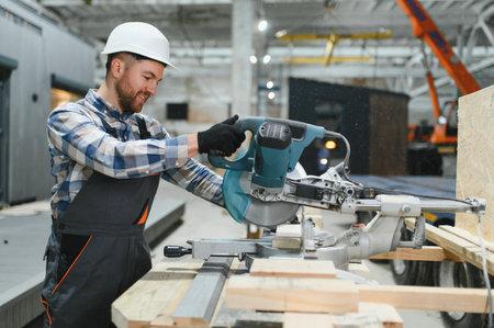 A carpenter cuts a wooden plank on a sawmill in a modular building factory, providing precise cuts...
