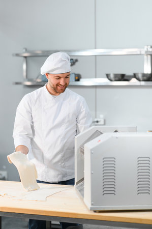 Concentrated at work. Handsome chef rolling a dough through pasta machine.