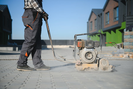 Landscaping worker using vibratory tamping machine plate compactor on a new patio driveway pavement...