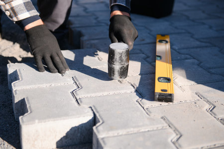 Close-up of construction worker installing and laying pavement stones on terrace, road or sidewalk. Worker using stones and rubber hammer to build stone sidewalk.の写真素材