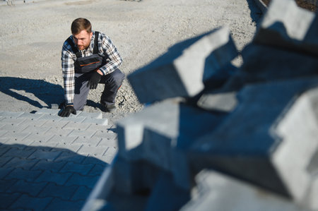 Builder laying a paving brick placing it on the sand foundation with gloved hands.