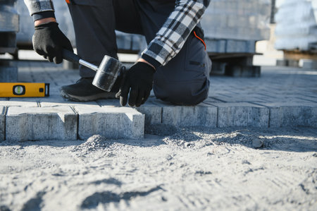 Close-up of construction worker installing and laying pavement stones on terrace, road or sidewalk. Worker using stones and rubber hammer to build stone sidewalk.の写真素材