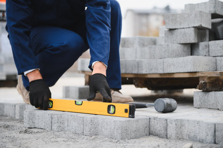 The master in gloves lays paving stones in layers. Garden brick pathway paving by professional paver...