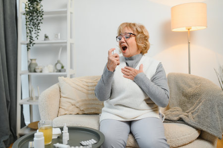 A woman is comfortably settled on her couch, using a soothing throat spray while surrounded by an array of tissues. Its the ideal home remedy for alleviating throat discomfort effectively.の写真素材