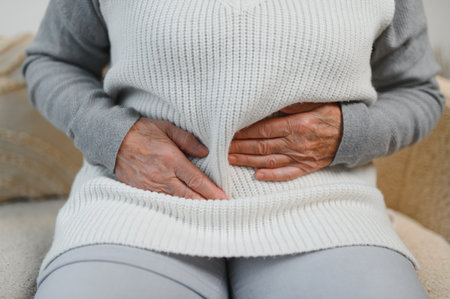 Mature woman suffering from stomach ache sitting on a bed in the bedroom. Senior woman sitting on her bed suffering from stomach ache at home.の写真素材