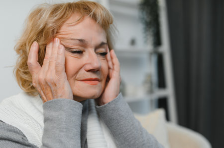 Senior woman sitting on a sofa at home with a headache, feeling pain and with an expression of being unwell.の写真素材