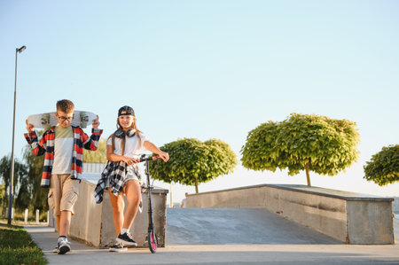 Satisfied children in the skate park. A boy with a skate and a girl with a scooter spend time together. Summer vacation.の写真素材