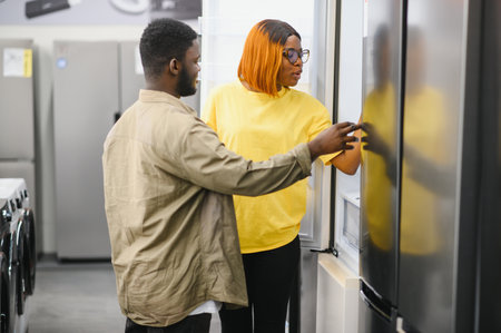 Young African American couple, satisfied customers choosing refrigerator in appliances store.の写真素材