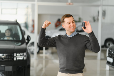 Handsome man customer holding key from auto, buying brand new car in showroom.の写真素材